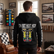 A man wearing a black hoodie with a large drag racing graphic on the back, standing in a garage-themed room with drag racing posters and tools on the wall.