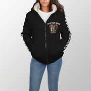 A woman wearing a black zip-up hoodie with a white sherpa-lined hood and a colorful graphic on the chest that reads 'I'M NOT MOST WOMEN'. The hoodie also has white text down one sleeve.