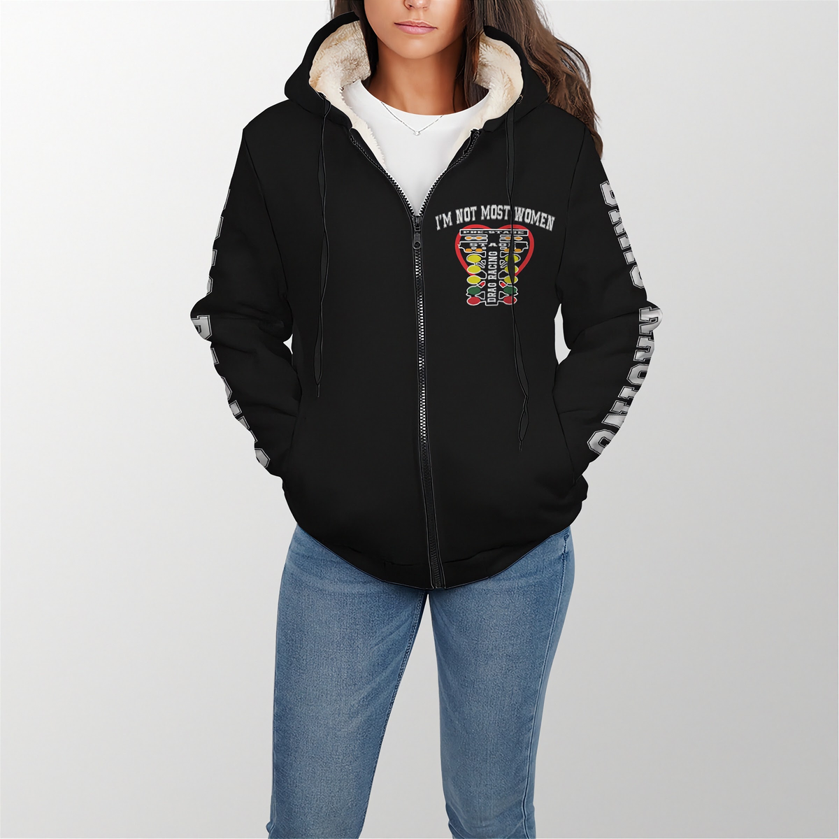 A woman wearing a black zip-up hoodie with a white sherpa-lined hood and a colorful graphic on the chest that reads 'I'M NOT MOST WOMEN'. The hoodie also has white text down one sleeve.