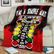 A black and red throw blanket draped over a beige sofa in a living room setting. The blanket features a bold graphic design with the text 'I'M A SIMPLE MAN' in white distressed letters, a vertical 'I LOVE BOOBS AND DRAG RACING' graphic, and a traffic light motif in red, yellow, and green.