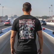 A man standing on a drag strip wearing a black t-shirt with a large back graphic that reads 'if you want to Drag Race' and features a detailed skull and engine design.