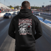 A man standing on a drag racing track, viewed from behind, wearing a black hoodie with a large graphic print on the back. The graphic features a skull, crossed bones, a red rose, and the text 'Drag Race' and 'You'll Need A Set of Vices'.