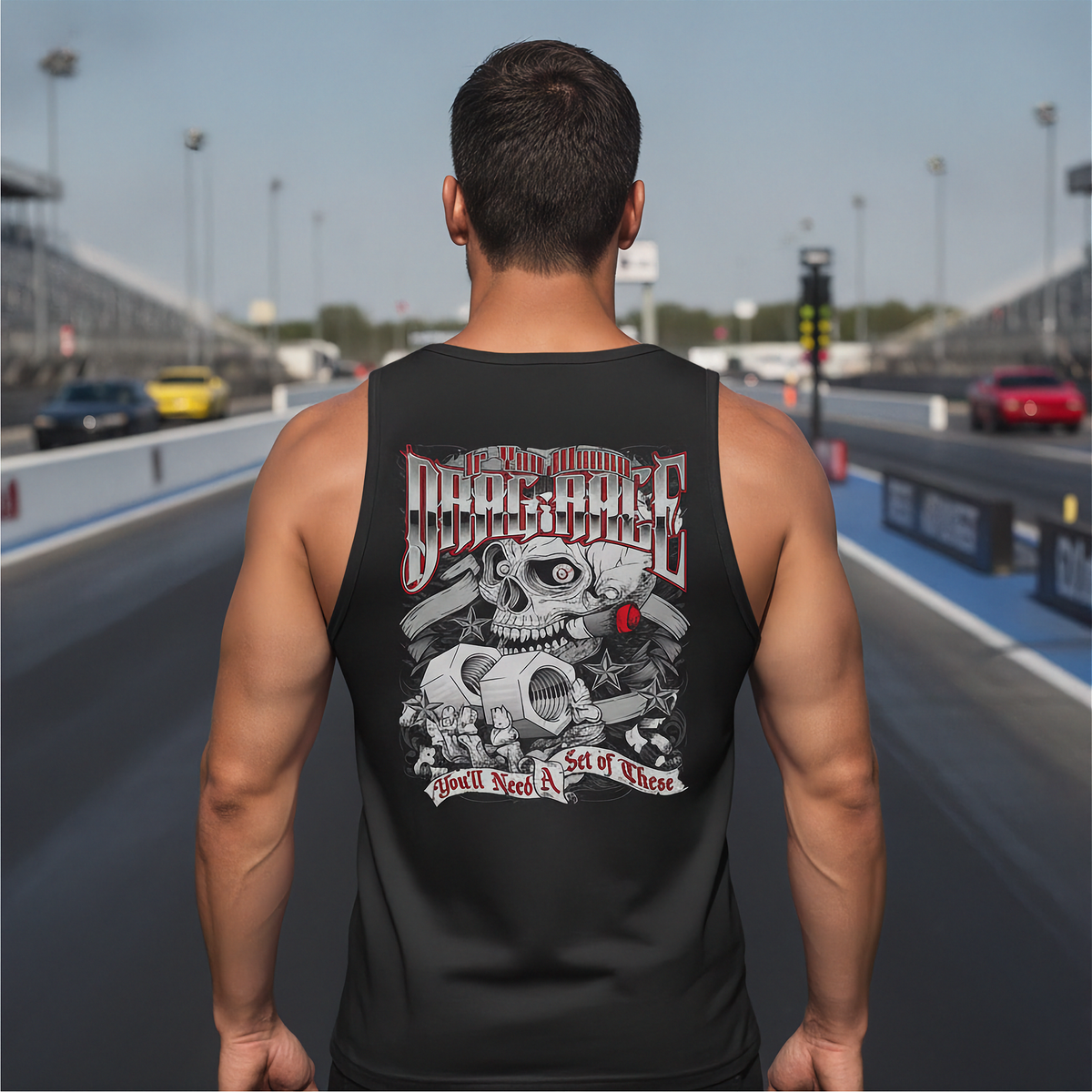 A man viewed from behind wearing a black tank top with a large graphic print on the back, standing on a racetrack.
