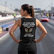 A woman stands on a racetrack wearing a black tank top with a humorous racing graphic on the back. The graphic features a white engine illustration and the text 'IF YOUR CAR DOESN'T SCARE YOU A LITTLE IT'S NOT FAST ENOUGH'.