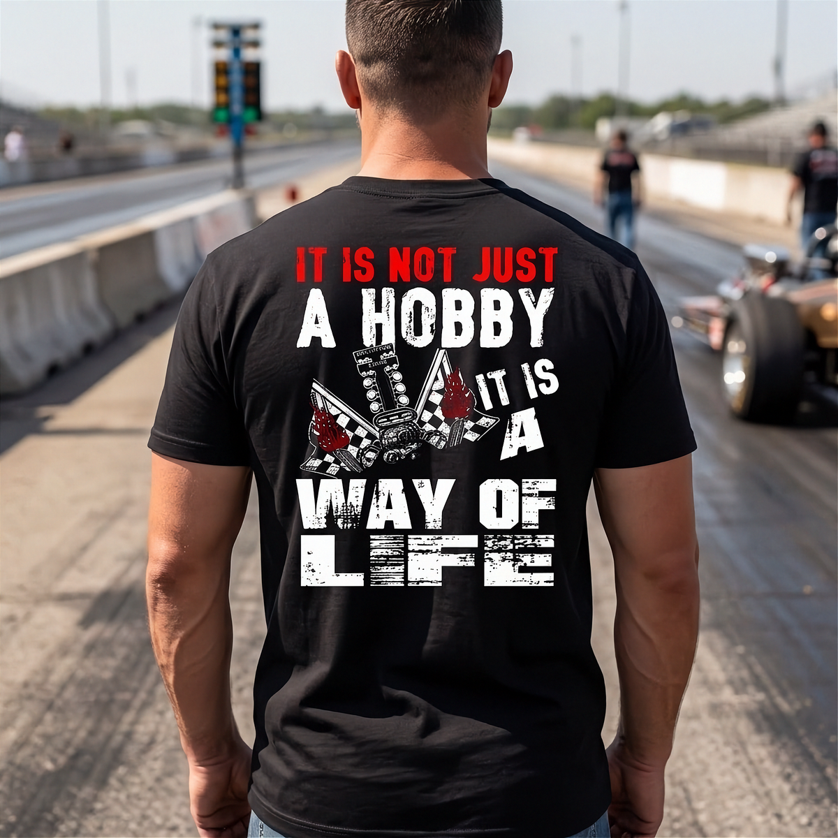 A man at a drag race track wearing a black shirt with 'It Is Not Just A Hobby IT'S MY WAY OF LIFE'