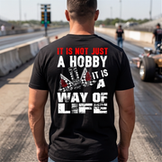 A man at a drag race track wearing a black shirt with 'It Is Not Just A Hobby IT'S MY WAY OF LIFE'
