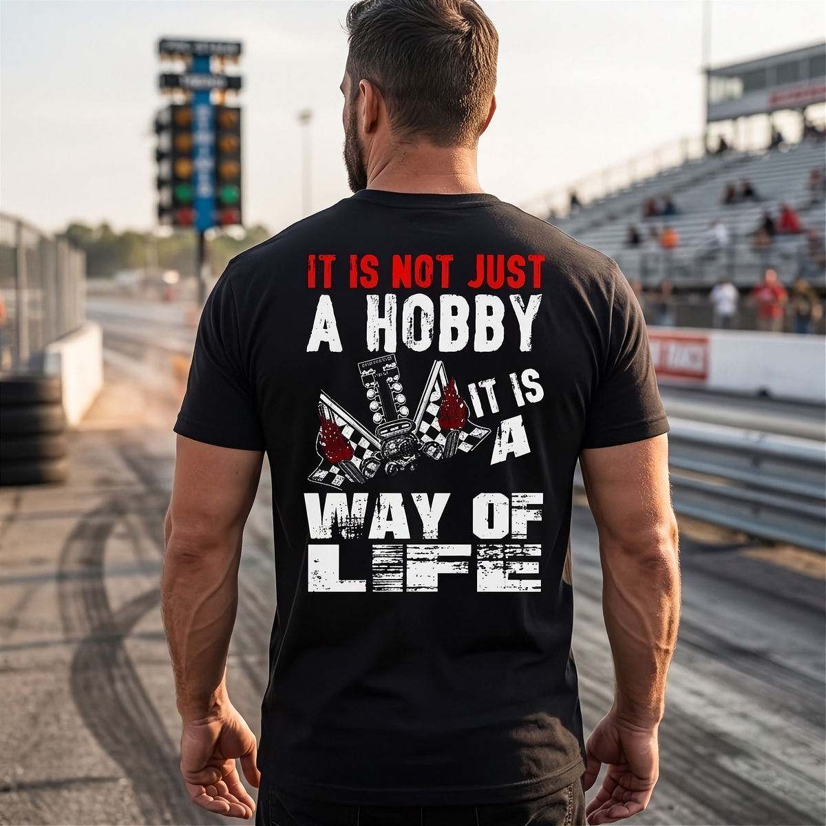 A man standing at a drag race track wearing a black shirt with 'It Is Not Just A Hobby IT'S MY WAY OF LIFE'