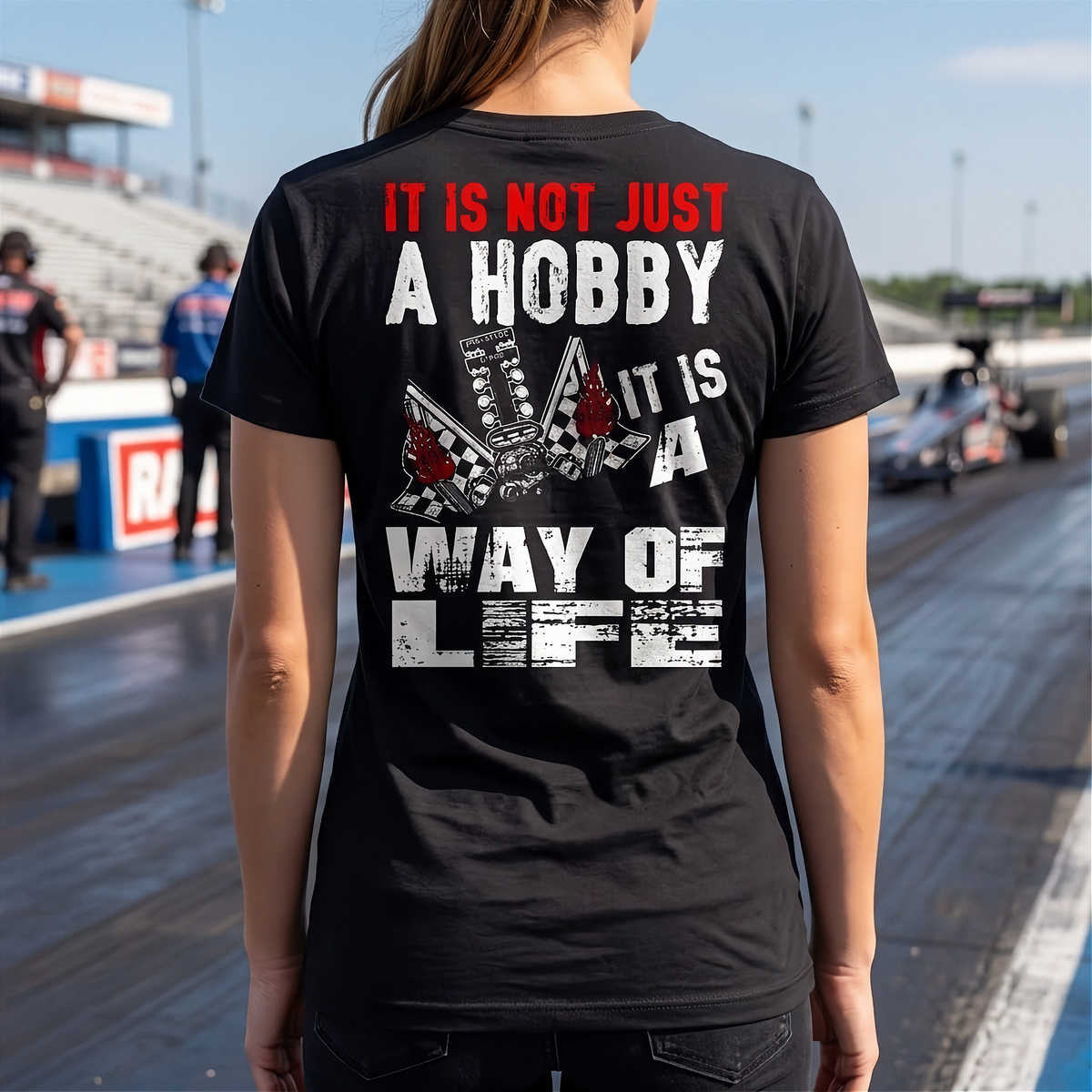 A woman at a drag race track wearing a black shirt with 'It Is Not Just A Hobby IT'S MY WAY OF LIFE'