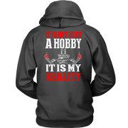 A dark gray hoodie shown from the back, featuring a graphic print with the text 'IT IS NOT JUST A HOBBY IT IS MY REALITY' in red and white, along with a small illustration of a ski jump and crossed skis.