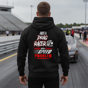 A man viewed from behind wearing a black hoodie with a large drag racing graphic on the back, standing on a racetrack with a car and grandstands in the background.