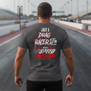 A man viewed from behind wearing a dark gray t-shirt with a red and white graphic that reads 'JUST A DRAG RACER WITH A SPEED PROBLEM' on a racetrack.