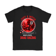 A black short-sleeve crewneck t-shirt featuring a graphic design on the front. The design shows a red full moon with a skeleton key, a black tree silhouette, dice, tombstones, and the text 'JUST A WITCH WHO LOVES DRAG RACING' in red and white.