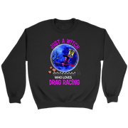 A black crewneck sweatshirt with a colorful graphic on the chest. The graphic features a witch riding a red racecar in front of a full moon with a haunted house and bare trees, with the text 'JUST A WITCH WHO LOVES DRAG RACING' in pink and white.