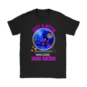 A black short-sleeve t-shirt with a colorful graphic print on the front. The graphic features a witch riding a red racecar on a broomstick in front of a large blue full moon, with jack-o'-lanterns and tombstones.