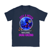 A navy blue short-sleeve t-shirt with a colorful graphic print on the front. The graphic features a witch riding a red racecar in front of a large blue full moon, with the text 'JUST A WITCH WHO LOVES DRAG RACING' in pink and white.
