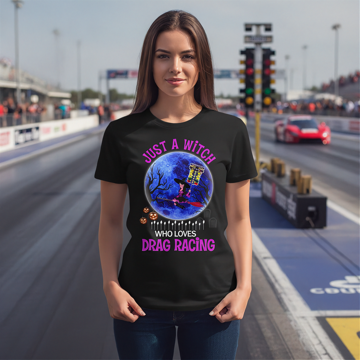 A woman stands on a drag racing track wearing a black graphic t-shirt with a Halloween-themed design featuring a witch's hat, pumpkin, and the text 'JUST A WITCH WHO LOVES DRAG RACING' in pink and white.