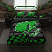 A green and black racing-themed bedding set, including a duvet cover and two pillowcases, displayed on a bed in a styled bedroom. The bedding features a bright green race car graphic, 'DIRT TRACK RACING' text, and a checkered pattern on a gray tire-strap background.