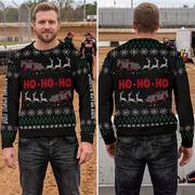 A man modeling a black Christmas sweater in a dirt arena, shown from the front and back. The sweater features a festive pattern with red 'HO-HO-HO' text, gray race cars, white snowflakes, and green zig-zag stripes.