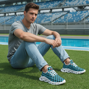 Man sitting on grass wearing blue checkered sneakers with a stadium in the background