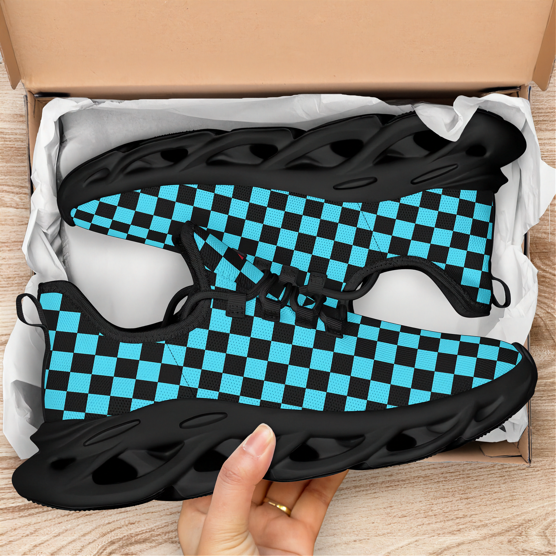 Black and blue checkered sneakers in a box with a hand holding one shoe.