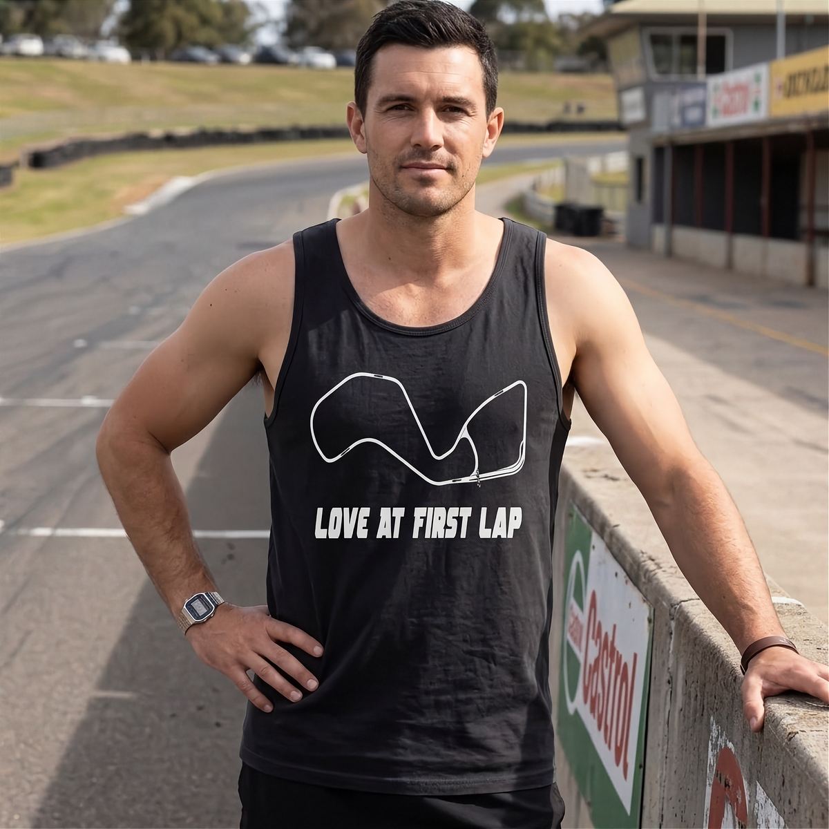 A man standing on a racetrack wearing a black tank top with a white track outline and the text 'LOVE AT FIRST LAP'.
