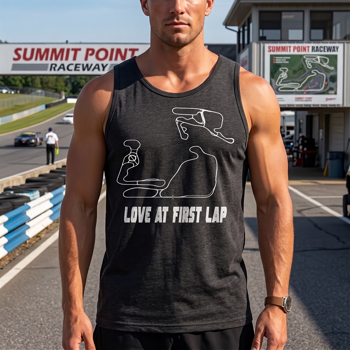 A man wearing a dark gray tank top with a white graphic of a racing track and the text 'LOVE AT FIRST LAP' standing on a race track with 'SUMMIT POINT RACEWAY' in the background.