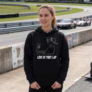 A woman wearing a black hoodie with a white graphic of a racing track and the text 'LOVE AT FIRST LAP' standing on a race track with 'SUMMIT POINT RACEWAY' in the background.