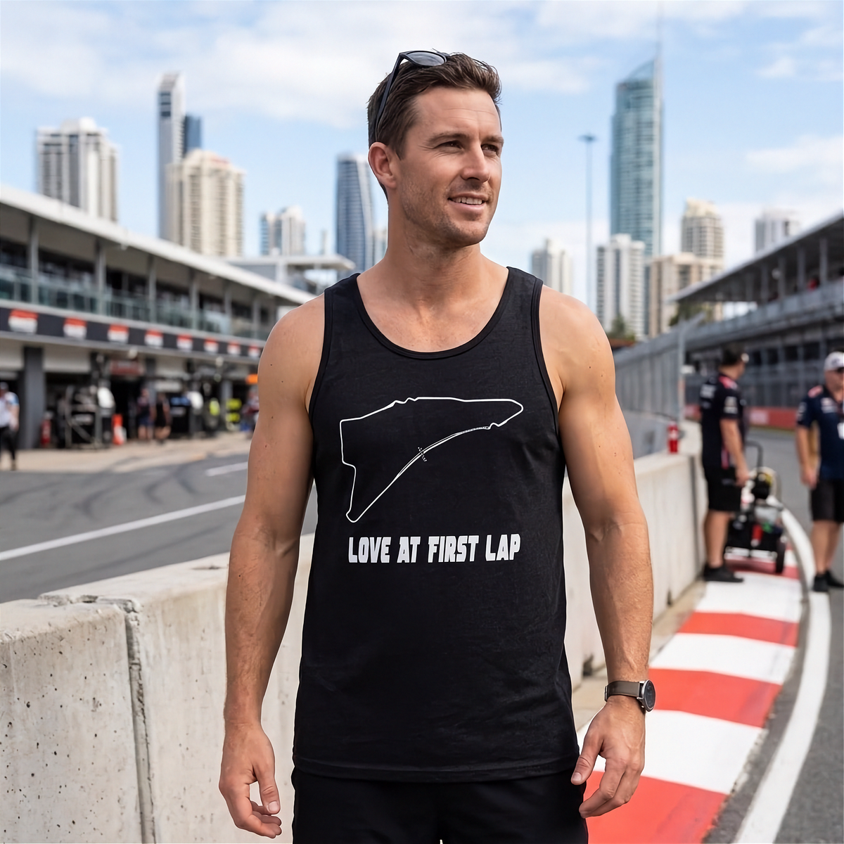 A man standing on a racetrack wearing a black tank top with a white outline of Victoria, Australia, and the text 'LOVE AT FIRST LAP'.