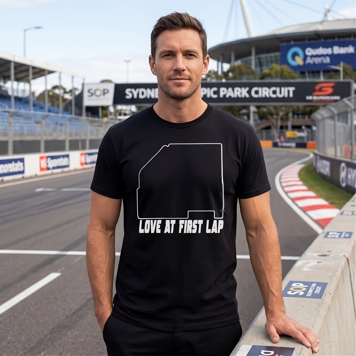 A man standing on a racetrack wearing a black t-shirt with a white outline of New South Wales and the text 'LOVE AT FIRST LAP'.