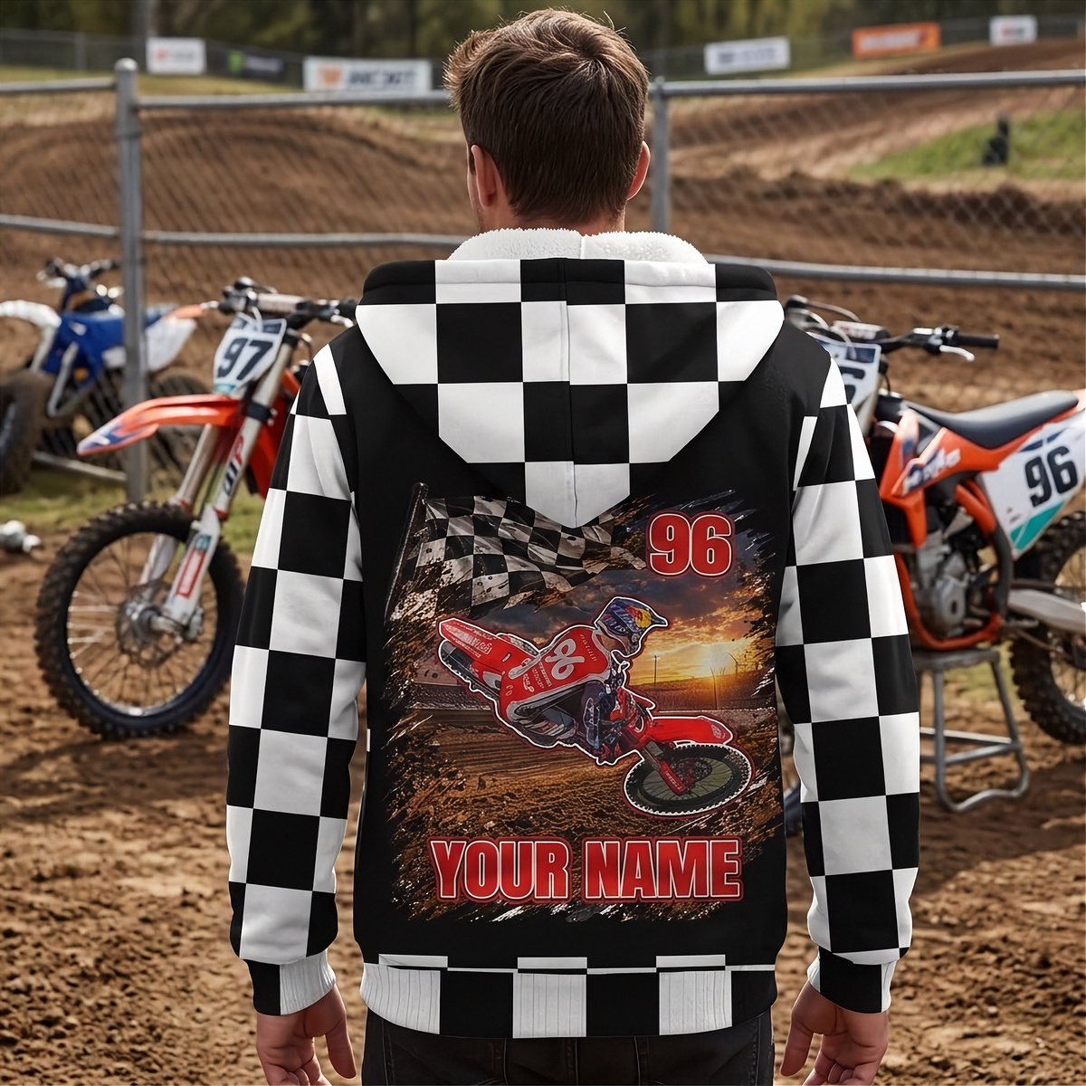 Man wearing a custom motocross sherpa jacket beside dirt bikes, showing the personalized back and checkered sleeves and hood.