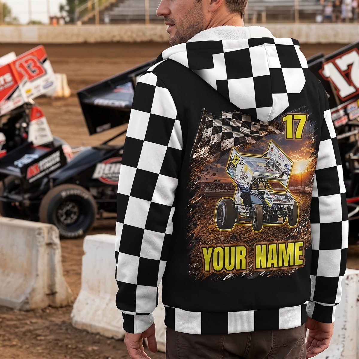 Man wearing a custom sprint car sherpa jacket beside race cars, showing the personalized back design and checkered sleeves.