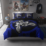 A motocross-themed bedding set featuring a duvet cover and two pillowcases with a large white and blue dirt bike graphic on a black and royal blue background, styled in a modern gray bedroom.
