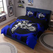 A bed dressed in a motocross-themed bedding set with a large black and blue duvet cover and matching pillowcases featuring a white and blue dirt bike graphic, shown in a styled bedroom setting.