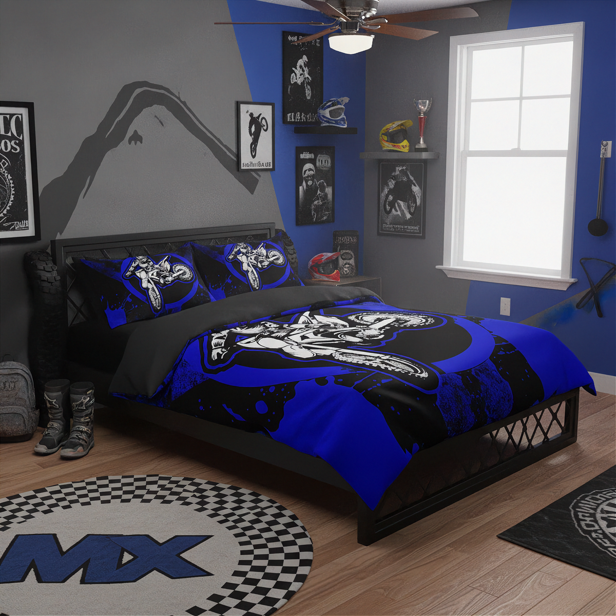 A blue, black, and white motocross-themed bedding set with matching pillowcases is displayed on a bed in a styled bedroom. The room features a gray and blue accent wall, a window, a ceiling fan, and various motocross-themed decor items including a checkered rug and framed posters.