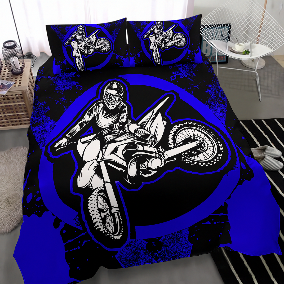 A motocross-themed bedding set featuring a duvet cover and two matching pillowcases with a bold graphic of a rider on a dirt bike over a black and royal blue background, shown in a bedroom setting.