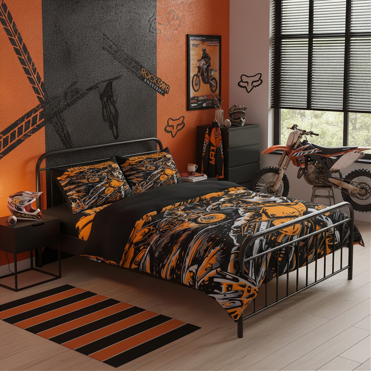 A motocross-themed bedroom featuring a black metal bed frame with a bold orange, black, and gray patterned comforter and matching pillow shams. The room has orange and dark gray accent walls with dirt track graphics, a framed motocross poster, a chest with a jersey, a helmet on a side table, and a dirt bike leaning near the window.