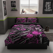 A bed dressed in a black and bright pink motocross-themed bedding set, shown in a styled bedroom with motocross wall art, a window, and boots on the floor.