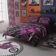 A bed dressed in a pink, black, and white graphic motorcycle-themed bedding set, shown in a styled bedroom with orange and blue walls, framed bike prints, a patterned rug, and a matching motorcycle rug.