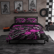 A motorcycle-themed bedding set with a bold pink and black graphic print, styled on a bed in a modern, dark-themed bedroom with motocross wall art, a tire, and dirt bike accessories.