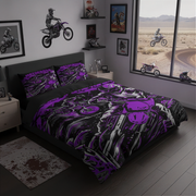 A bed dressed in a bold purple, black, and gray graphic duvet cover and matching pillowcases, styled in a dark modern bedroom with motorcycle wall decals, framed art, and a large window showing a desert landscape.
