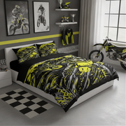 A bed dressed in a black and neon yellow motocross-themed bedding set, styled in a modern bedroom with a white headboard, matching pillows, wall decals, a motorcycle, and motocross gear.
