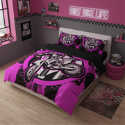 A kids' bed styled in a pink and gray room, featuring a black and hot pink motocross graphic duvet cover and matching pillowcases. The room is decorated with a neon-style 'DIRT BIKE LIFE' sign, a 'NO FEAR' poster, and a small toy motorcycle on a shelf.