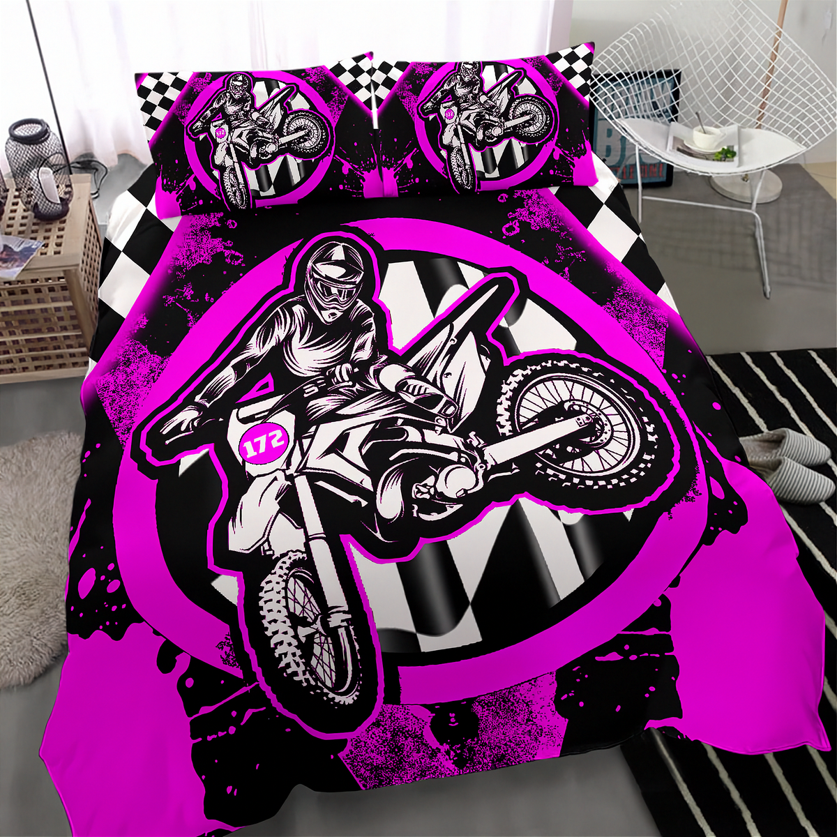A motocross-themed bedding set featuring a duvet cover and two matching pillowcases with a bold graphic of a rider on a dirt bike over a black-and-white checkered background, accented by bright pink splatter and circular logo designs.