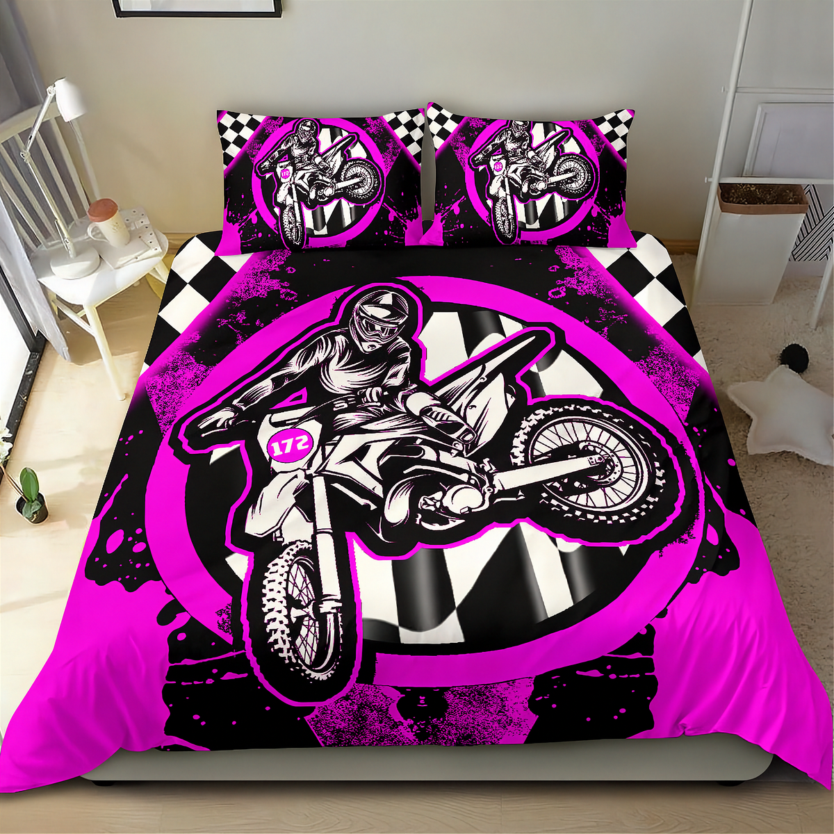 A bed dressed in a motocross-themed bedding set with a duvet cover and two pillowcases, featuring a large black, white, and neon pink graphic of a rider on a dirt bike, with checkered and circular design elements, shown in a bedroom setting.