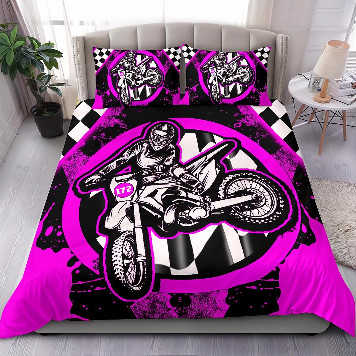 A bed dressed in a motocross-themed bedding set featuring a large black, white, and neon pink graphic of a rider on a dirt bike, with matching pillowcases, shown in a styled bedroom setting.