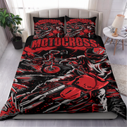 A bed dressed in a motocross-themed bedding set with a duvet cover and two matching pillowcases, shown in a styled bedroom setting with a headboard, side table, lamp, and plant.
