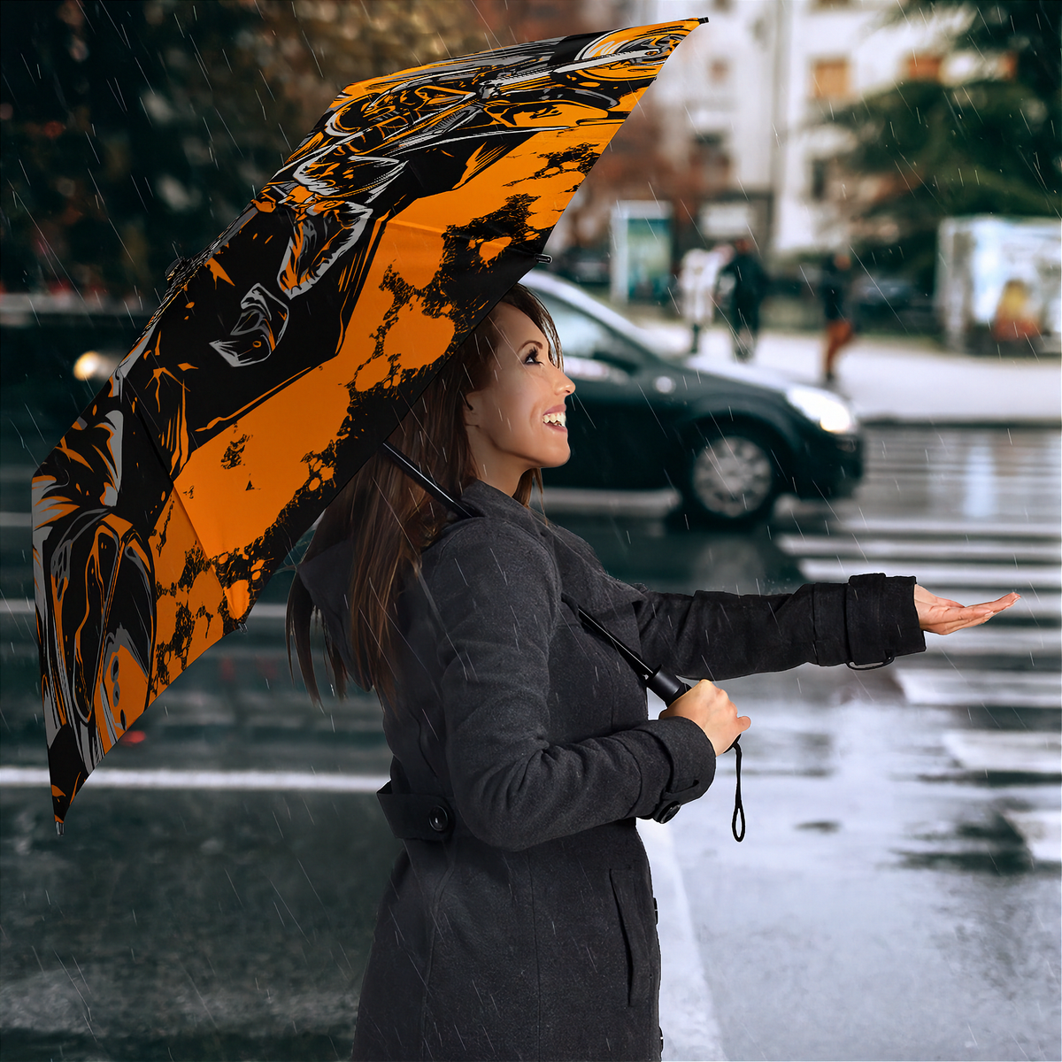 A woman in a dark gray coat stands in the rain on a city street holding an open umbrella with a bold black and orange graphic pattern.