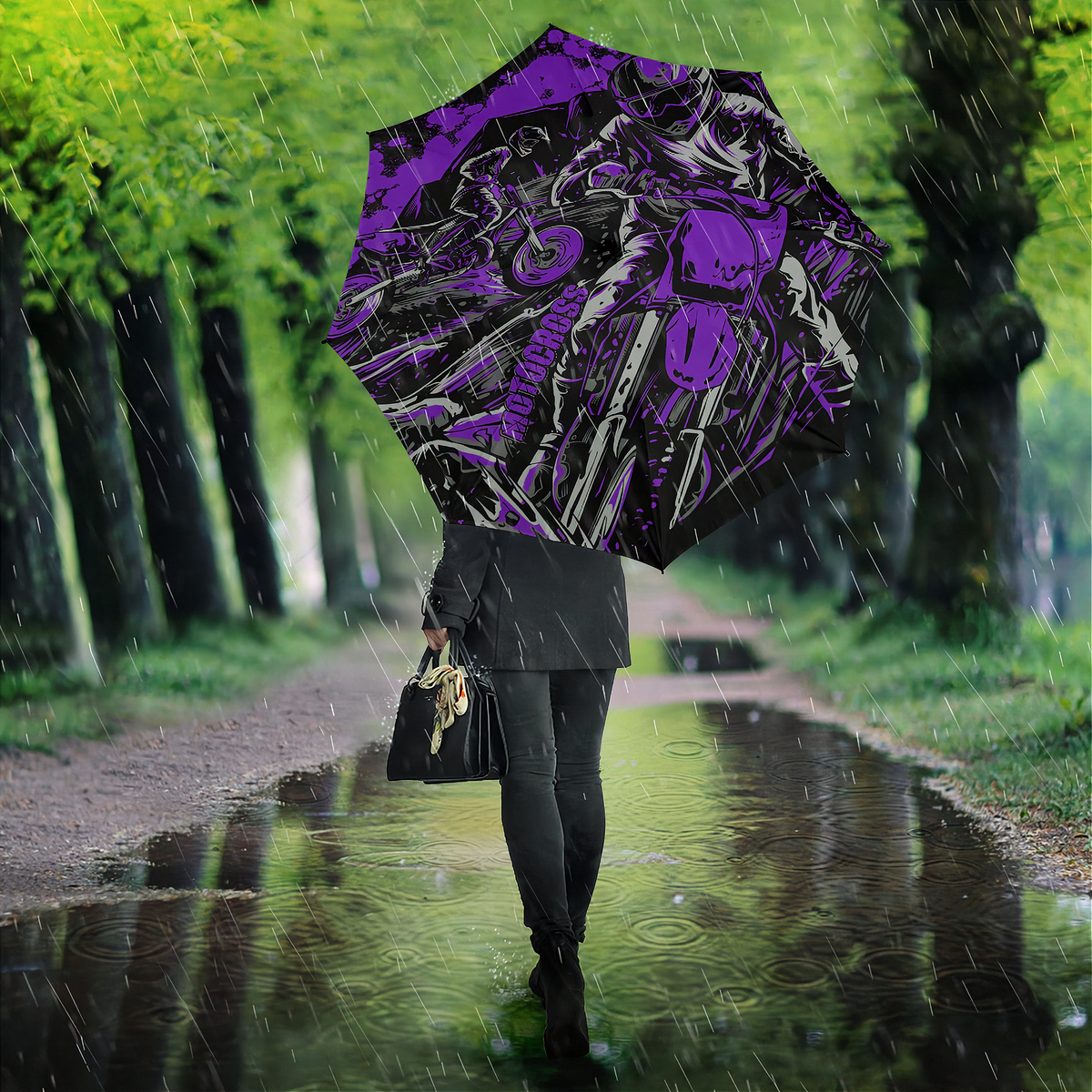 A person walking in the rain along a tree-lined path, holding a large open umbrella with a bold purple and black graphic print featuring a motorcycle and rider illustration.