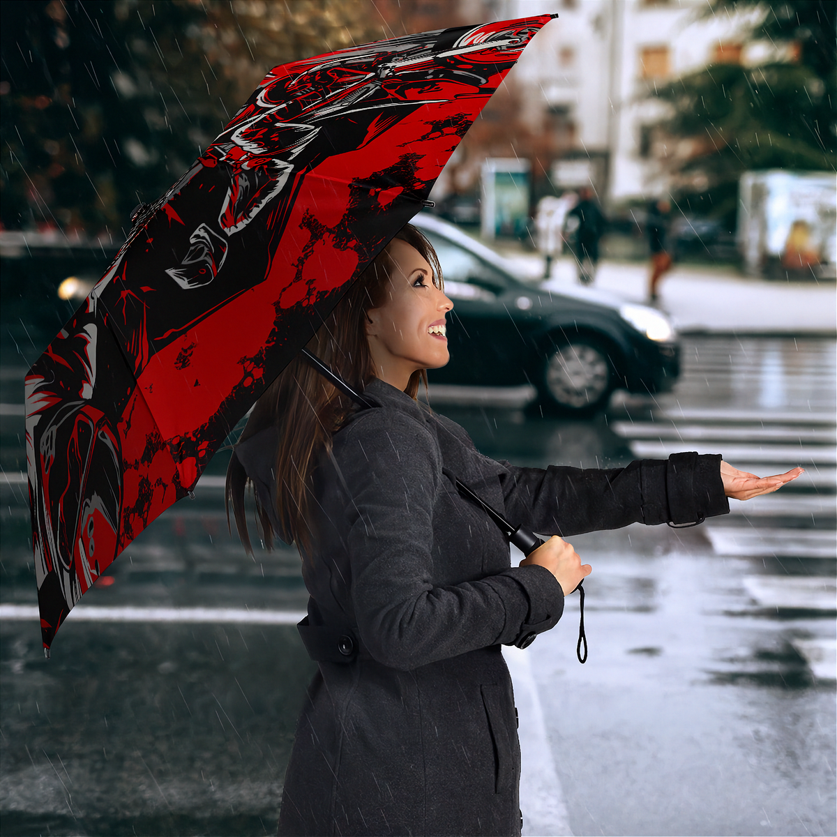 A woman in a dark gray coat stands in the rain holding a large open umbrella with a bold red and black graphic print featuring a wolf or dragon design. The background shows a blurred city street with cars and buildings.
