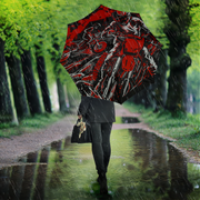 A person walking in the rain on a tree-lined path holding a large open umbrella with a red, black, and white motorcycle graphic print.